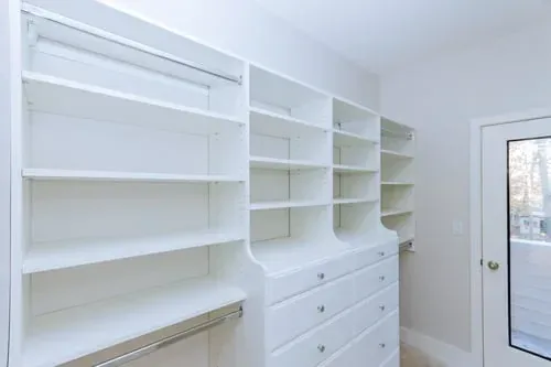 Clean white storage shelving system with open shelves and a built-in drawer tower