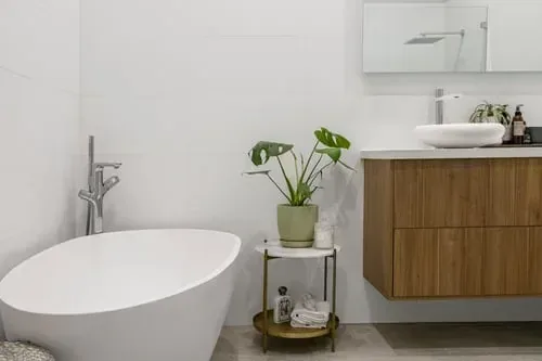 Bright organized bathroom with a wood vanity, rolled towels on a tiered cart and a green plant