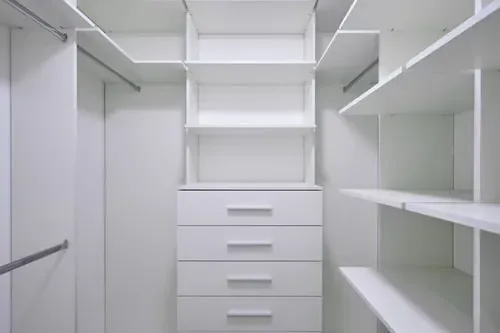 Bright empty walk-in closet with white shelving and a built-in drawer tower