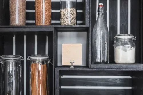Dark open shelving holding labeled glass jars of pasta, grains and dry goods with a wooden label tag