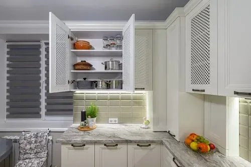 Cream kitchen cabinet opened to reveal neatly organized cookware and dry goods